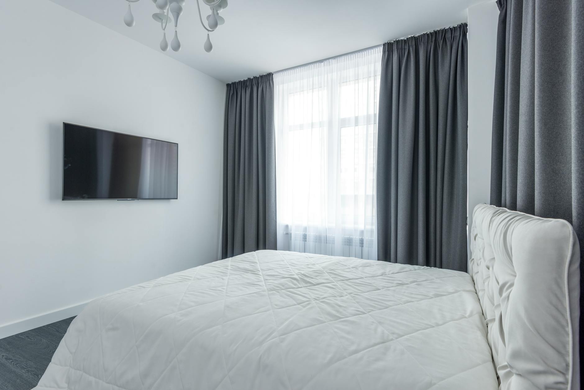 Minimalistyczna sypialnia z TV i eleganckimi zasłonami przy oknie